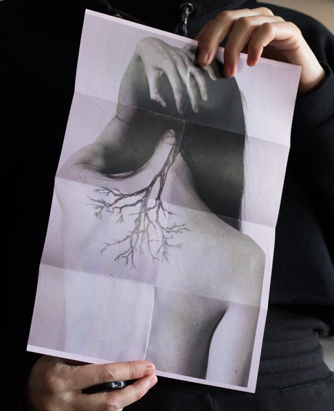 Tangled 1 - hands holding a black and white photograph of a tree tatooed on a person's neck, printed on a creased purple paper